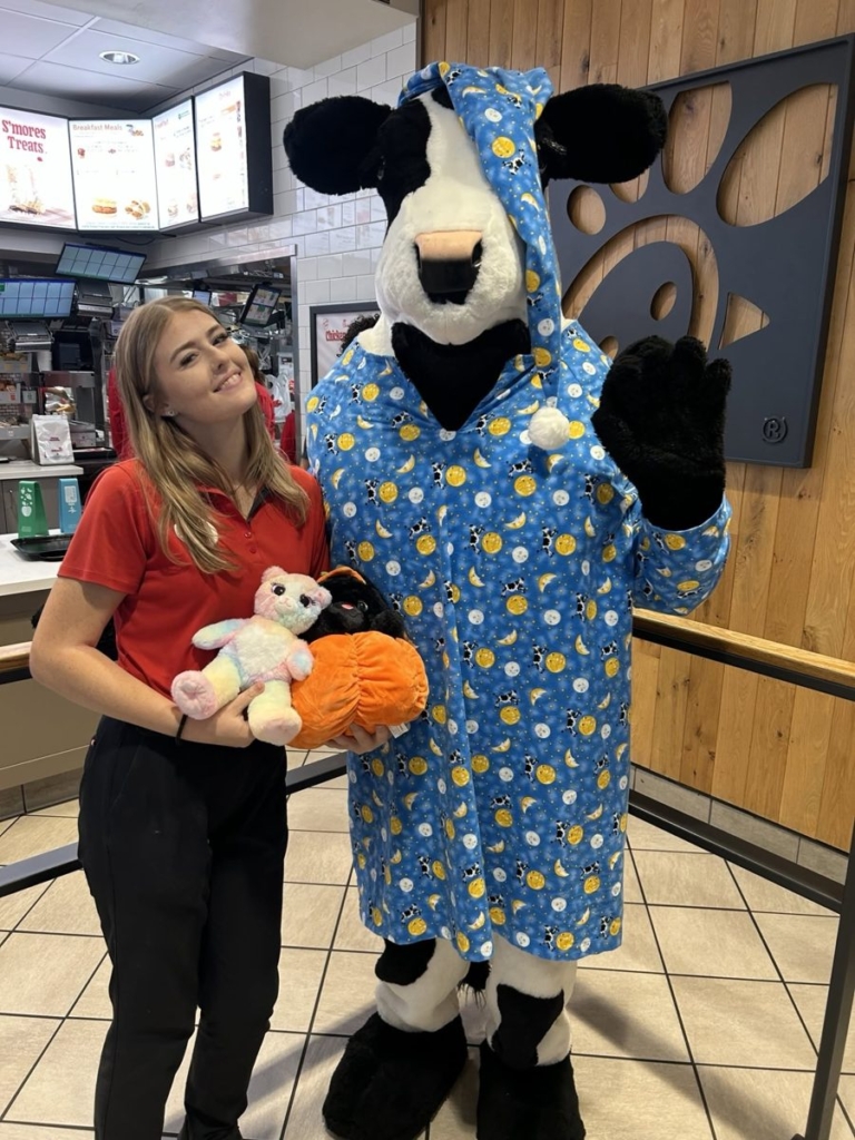 Chick-fil-A Cow mascot holding two stuffed animals in a pumpkin
